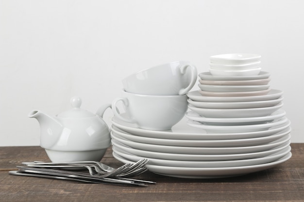 Ein Stapel Geschirr. Geschirr auf einem braunen Holztisch. Teller und Besteck, Tassen und Wasserkocher.