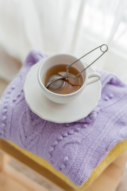 Ein Stapel gestrickter Kleidung auf einem Holzstuhl, eine Tasse heißen Tee