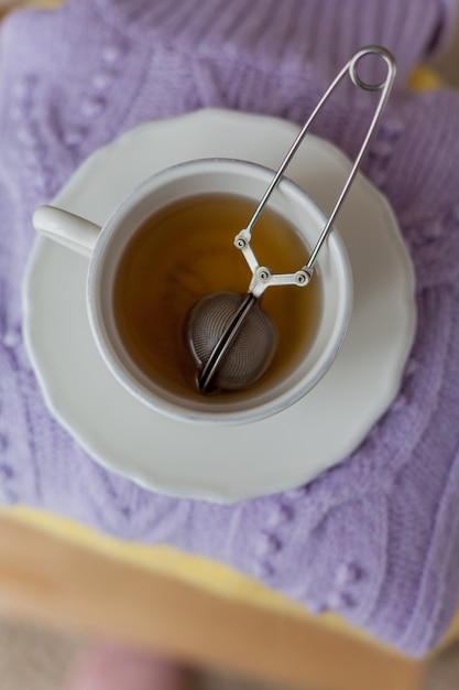 Ein Stapel gestrickter Kleidung auf einem Holzstuhl, eine Tasse heißen Tee