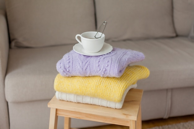 Ein Stapel gestrickter Kleidung auf einem Holzstuhl, eine Tasse heißen Tee