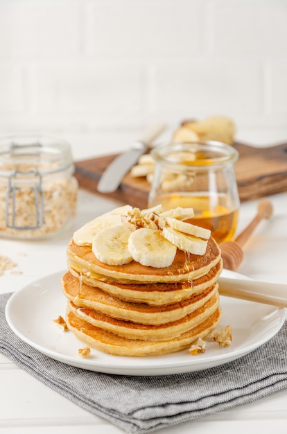 Ein Stapel Haferflocken-Bananen-Pfannkuchen mit Scheiben von frischen Bananen, Walnüssen und Honig mit einer Tasse Tee