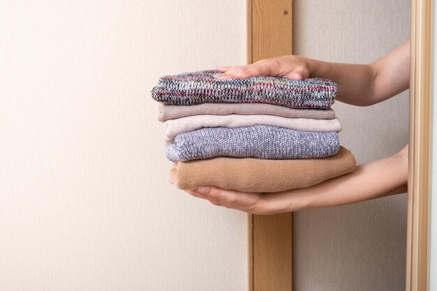 Ein Stapel kuscheliger Strickpullover in Frauenhänden wird aus dem Kleiderschrank Warm Concept genommen