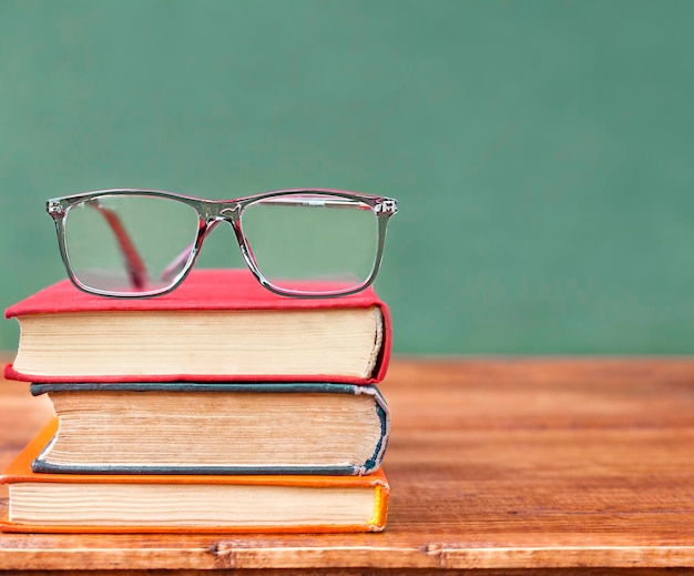 ein Stapel mehrfarbiger Bücher mit Brille, Nahaufnahme auf grünem Hintergrund mit Kopierraum