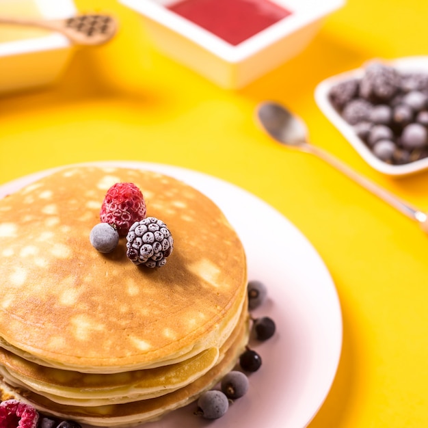 Ein Stapel Pfannkuchen auf einer rosa Platte mit Beeren nahe bei Honig- und Erdbeermarmelade