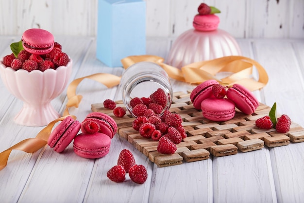 Ein Stapel rosa Macarons, umgeben von Himbeeren auf einem Holztisch