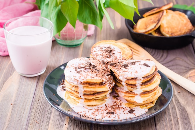 Ein Stapel von den Pfannkuchen angefüllt mit Fruchtjoghurt und mit Schokoladenraspel auf einer Platte auf einem Holztisch besprüht