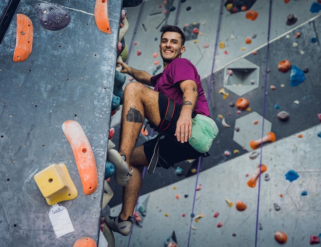 Ein starker Kletterer klettert auf eine künstliche Wand mit farbenfrohen Griffen und Seilen