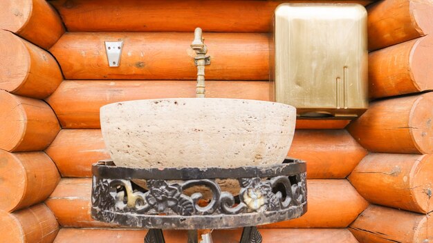 Ein Steinwaschbecken auf einem metallgeschmiedeten Ständer in einem Blockhaus. Interieur in einem Haus aus Holz.