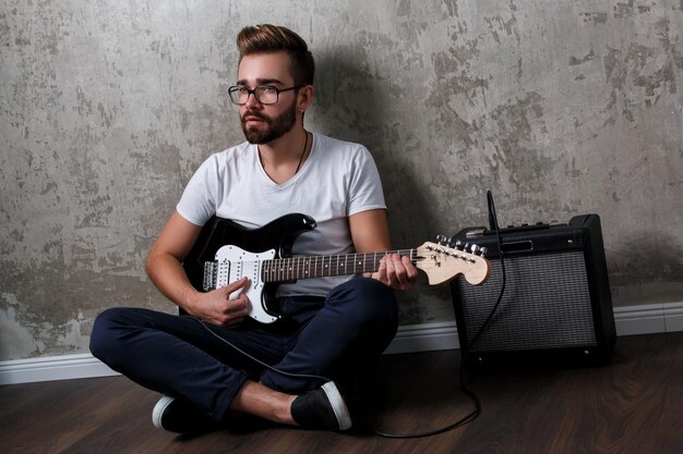 Foto ein stilvoller bärtiger typ mit gitarre gegen eine betonwand