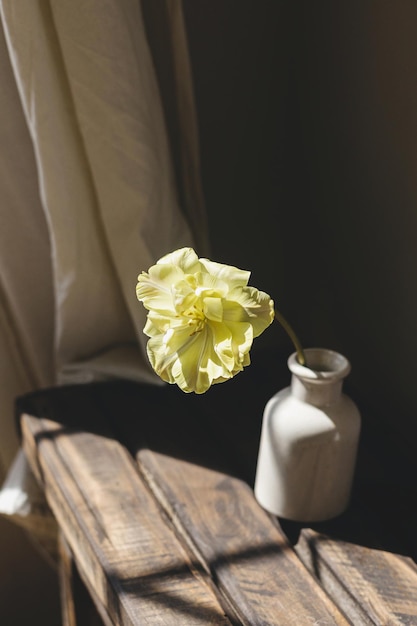 Ein stilvoller Frühlingsbouquet auf einer rustikalen Holzbank Schöne gelbe Tulpe in einer Vase im Sonnenlicht auf dem Hintergrund von grauen Wänden und Leinenvorhängen Blumenstillleben Glücklicher Muttertag