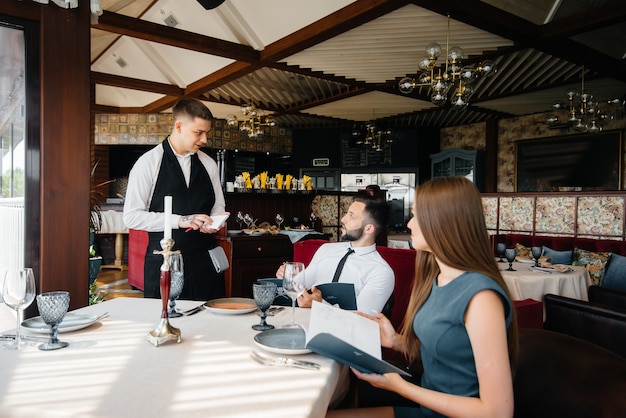 Ein stilvoller Kellner bedient ein junges Paar, das sich in einem Gourmetrestaurant verabredet hat. Kundenservice in der Gastronomie.