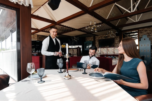 Ein stilvoller Kellner bedient ein junges Paar, einen Mann und eine Frau, die zu einem Date in ein Gourmetrestaurant gekommen sind Kundenservice in den Restaurants und Catering-Betrieben