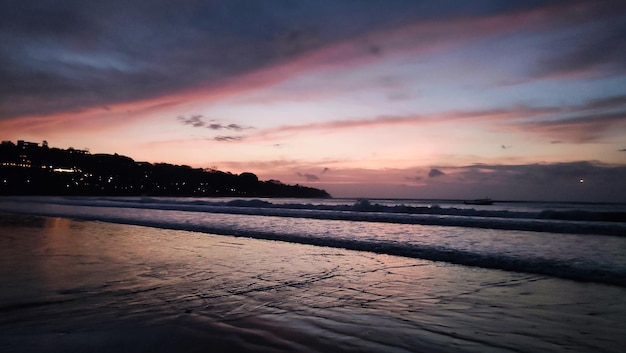 Ein Strand bei Sonnenuntergang mit einem rosa und orangefarbenen Himmel.