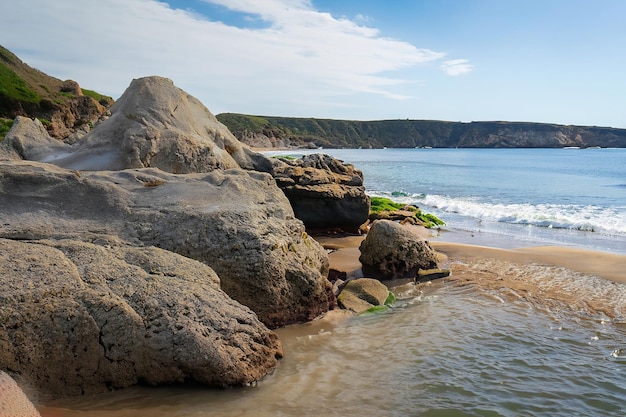 Ein Strand mit einem Felsvorsprung und einem großen Felsen auf der rechten Seite.