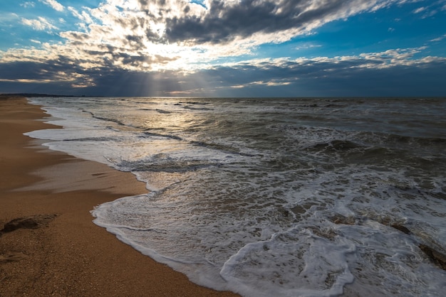 Ein Strand mit goldenem Sand, kleinen Wellen und einem wunderschönen dramatischen Himmel