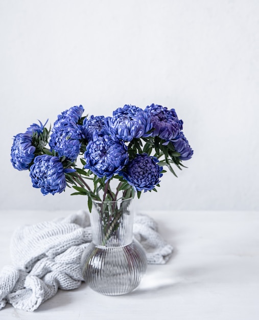 Ein Strauß blauer Chrysanthemen in einer Glasvase und ein gestricktes Element auf weißem Hintergrund, Kopierraum.