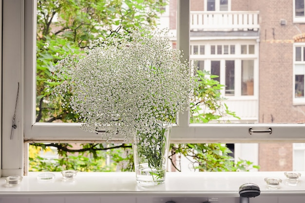 Ein Strauß frischer weißer Frühlings-Gypsophila in einer Vase, die an einem sonnigen Tag auf einem Fensterbrett steht.