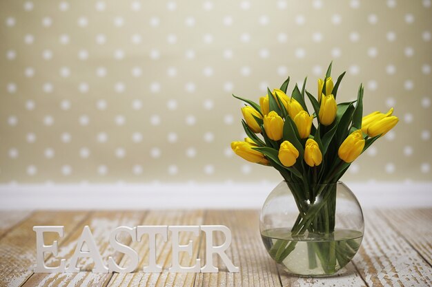 Ein Strauß gelber Tulpen in einer Vase auf dem Boden. Ein Geschenk zum Tag einer Frau aus gelben Tulpenblumen. Schöne gelbe Blumen in einer Vase an der Wand.