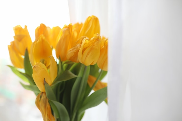 Ein Strauß gelber Tulpen in einer Vase auf der Fensterbank. Ein Geschenk zum Tag einer Frau aus gelben Tulpenblumen. Schöne gelbe Blumen in einer Vase am Fenster.