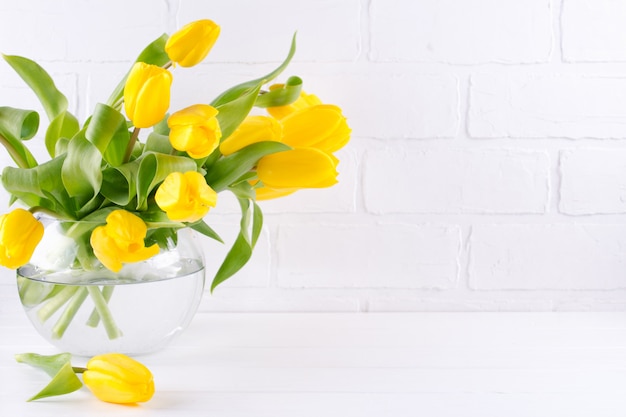 Ein Strauß gelber Tulpenblumen in der Glasvase auf weißem Hintergrund. Ein Geschenk an den Tag einer Frau. Speicherplatz kopieren.