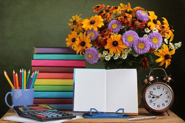 Ein Strauß Herbstblumen, ein Wecker und ein offenes Buch auf einem Ständer.