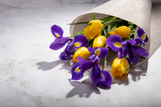 Ein Strauß Iris und Tulpen in einer Leinwand auf dem Tisch.