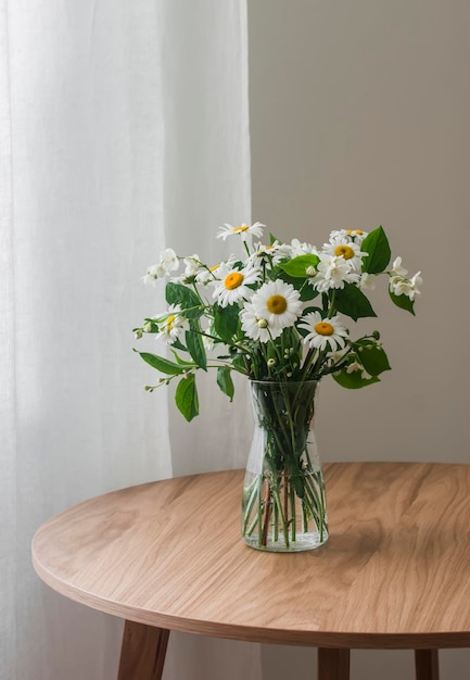 Ein Strauß Jasmin und Kamille auf einem runden Holztisch im Wohnzimmer