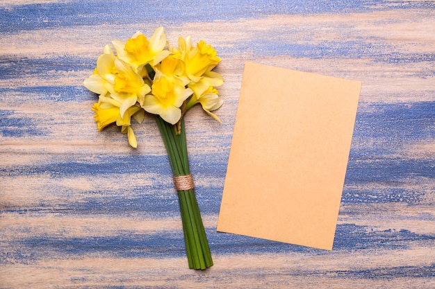 Ein Strauß Narzissen und ein Blatt Papier auf Holzgrund