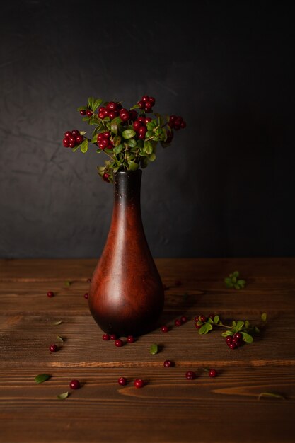 Ein Strauß Preiselbeeren in einer Vase auf einer Holzoberfläche auf einem dunklen Hintergrund