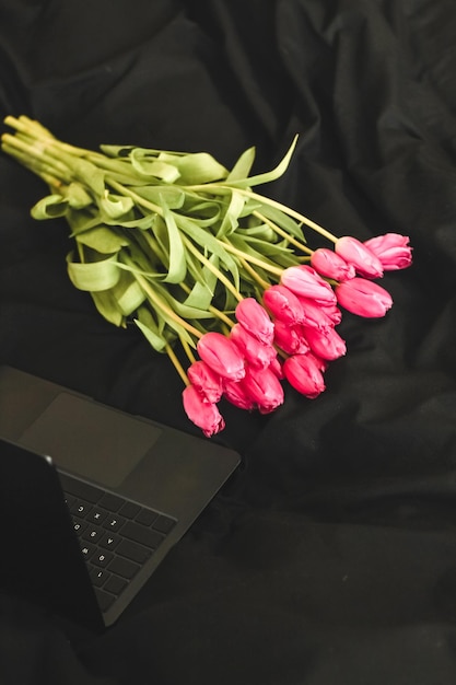 Ein Strauß rosa Blumen auf schwarzem, stilvollem Leinen mit einem offenen Laptop