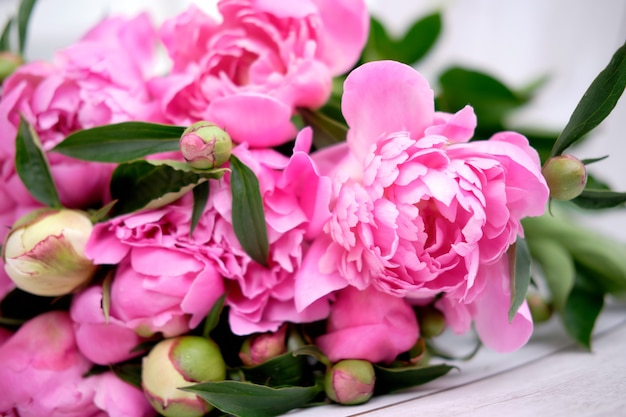 Ein Strauß rosa purpurroter Pfingstrosen liegt hautnah auf einem Holztisch