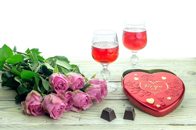 Ein Strauß rosa Rosen, Weingläser und eine Schachtel mit herzförmigen Bonbons