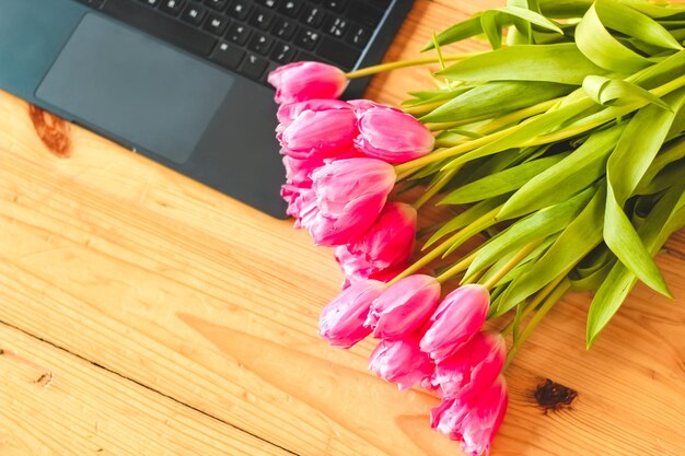 Ein Strauß rosa Tulpen blüht auf einem Hintergrund aus Brettern mit einem offenen Laptop