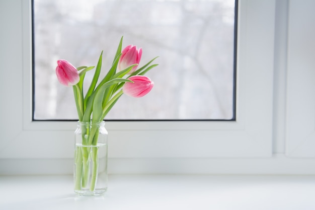 Ein Strauß rosa Tulpen in einem Glas befindet sich auf der Fensterbank im Haus.