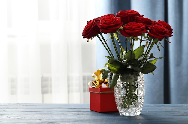 Ein Strauß roter Rosen in einer Vase und eine Geschenkbox auf dem Tisch. Liebeserklärung. Valentinstag Feier
