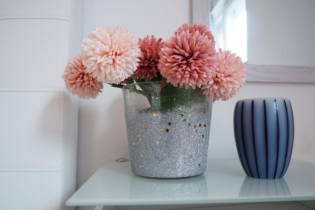 Ein Strauß schöner rosa Kunstblumen auf einem weißen Tisch im Schlafzimmer Innenarchitektur Innenarchitektur des Frauenschlafzimmers Blumenstrauß in einer Vase Aromatische gestreifte Kerze Spiegel an der Wand