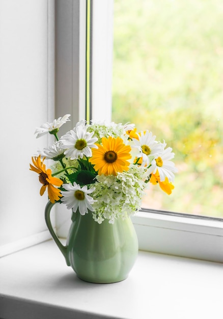 Ein Strauß Sommerblumen aus Gänseblümchen Hortensien in einem Vintage-Keramikkrug am Fenster in einem hellen Raum