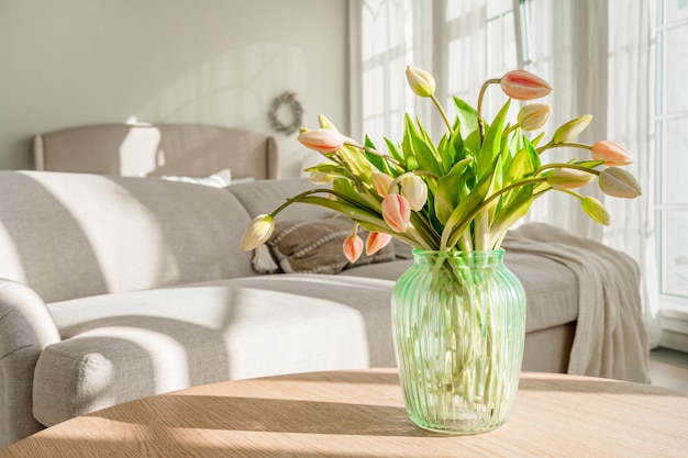 Ein Strauß Tulpen in einer schönen Vase zu Hause in einem hellen, modernen Interieur auf einem Holztisch