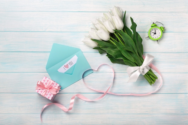 Ein Strauß weißer Tulpen und ein rosa Band in Form eines Herzens mit einer Geschenkbox