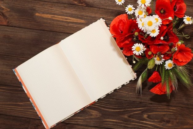 Ein Strauß Wildblumen: Gänseblümchen und Mohn auf einem Holztisch mit einem Notebook.