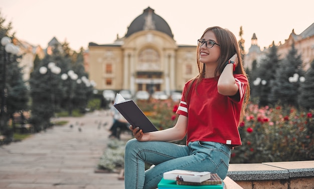 Ein Student im roten T-Shirt sitzt mit offenem Notizblock auf der Stufe und schaut lächelnd zur Seite