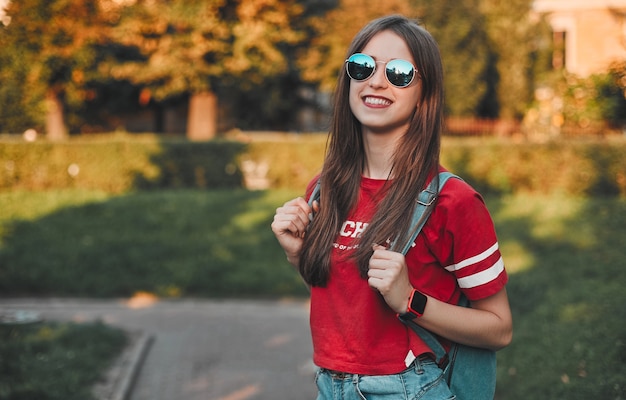 Ein Student in einem roten T-Shirt mit einem Rucksack mit Sonnenbrille auf der Straße