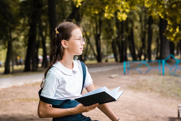 Ein Student mit Brille ist vom Lesen eines Buches abgelenkt und schaut an einem warmen Tag im Park weg