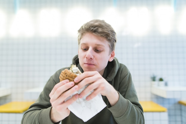 Ein Student mit einem hungrigen Blick sieht einen Hamburger in seinen Händen an.