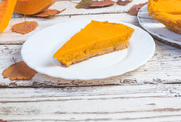 Ein Stück amerikanischer Kürbiskuchen und Kürbis auf einem weißen Holztisch Traditionelles Herbstessen