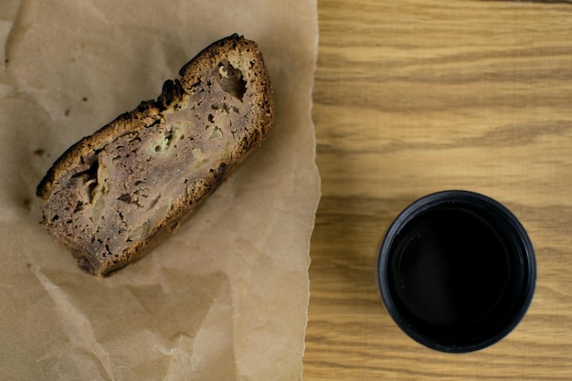 Ein Stück Brot liegt auf einem Blatt Papier neben einer Tasse Kaffee.