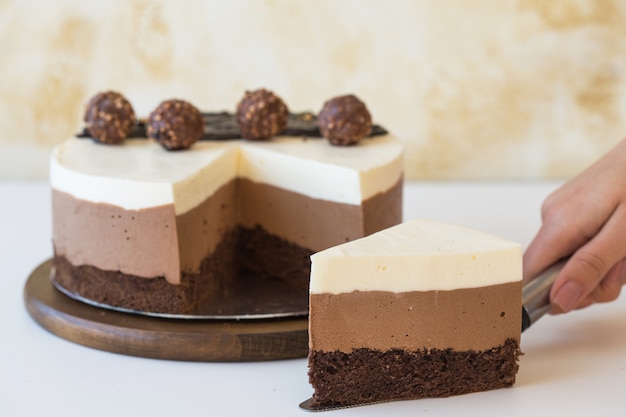 Ein Stück eines Mousse-Kuchens "Drei Schokolade" in der Hand eines Mädchens, bestreut mit geriebener Schokolade und dekorierten Süßigkeiten