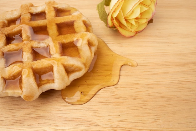 Ein Stück frische Waffel mit Honig auf einem Holzbrett.