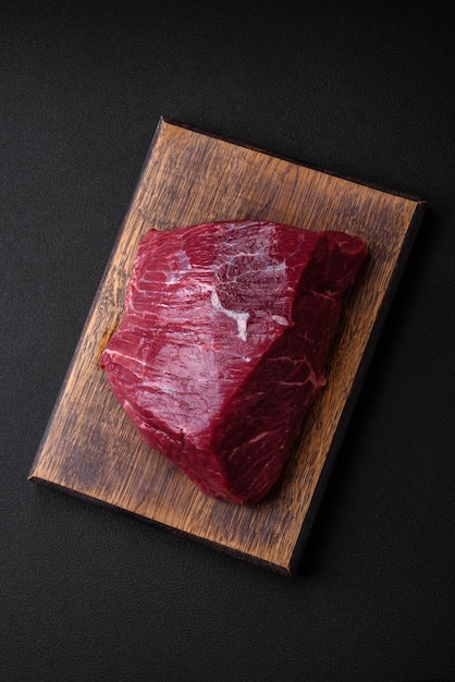 Ein Stück frisches rohes Rindfleisch mit Salzgewürzen und Kräutern auf einem Holzschneidebrett