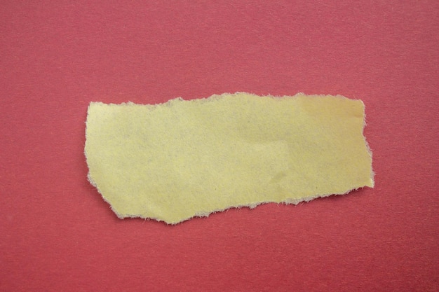 Ein Stück gelbes zerrissenes Papier wird von einem roten Hintergrund abgerissen.